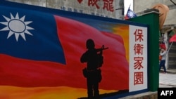 Seorang turis (kanan) berjalan melewati mural yang dilukis di dinding Kepulauan Kinmen Taiwan, yang terletak hanya 3,2 km dari pantai daratan China. (Foto: AFP)