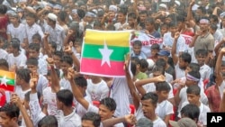 Rohingya refugees gather in the rain, with a flag of Myanmar seen at center, to demand safe return to Myanmar's Rakhine state as they mark the seventh anniversary of their exodus at their refugee camp in Cox's Bazar district, Bangladesh, Aug. 25, 2024. 