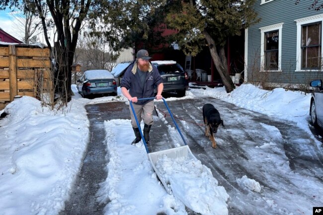 Harold Merrimont shovels heavy, wet snow alongside his dog in Plainfield, Vermont, Jan. 10, 2024.