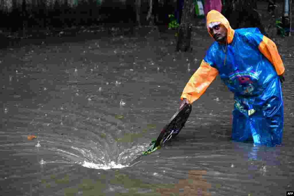 A municipal worker stands to guide vehicles away from a manhole along a flooded street during rainfall in Mumbai, India.