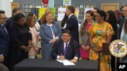 In this screenshot from a livestream broadcast by the State of Illinois, Gov. J.B. Pritzker signs a bill, June 12, 2023, at Harold Washington Library's Thomas Hughes Children's Library in downtown Chicago. (State of Illinois via AP)