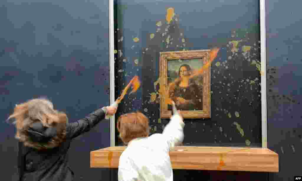 This image grab taken from AFPTV footage shows two environmental activists from the collective dubbed &quot;Riposte Alimentaire&quot; (Food Retaliation) hurling soup at Leonardo Da Vinci&#39;s &quot;Mona Lisa&quot; painting, at the Louvre museum in Paris.