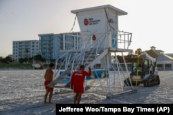 From left, Matthew Blowers and Patrick Brafford prepare to secure a lifeguard tower in preparation for a potential storm at Clearwater Beach in Clearwater, Florida, Aug. 3, 2024. (Jefferee Woo/Tampa Bay Times via AP)