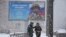 A woman talks to a boy as they walk under a snowfall past a billboard with a portrait of a Russian soldier awarded for action in Ukraine and the words "Glory to the heroes of Russia", in St. Petersburg, Russia, Feb. 10, 2023