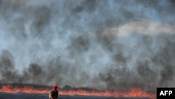 A protester walks past a wildfire started by a police-launched tear gas canister during a march as part of a rally against the construction of giant water reservoir near in Migne-Auxances, western France.