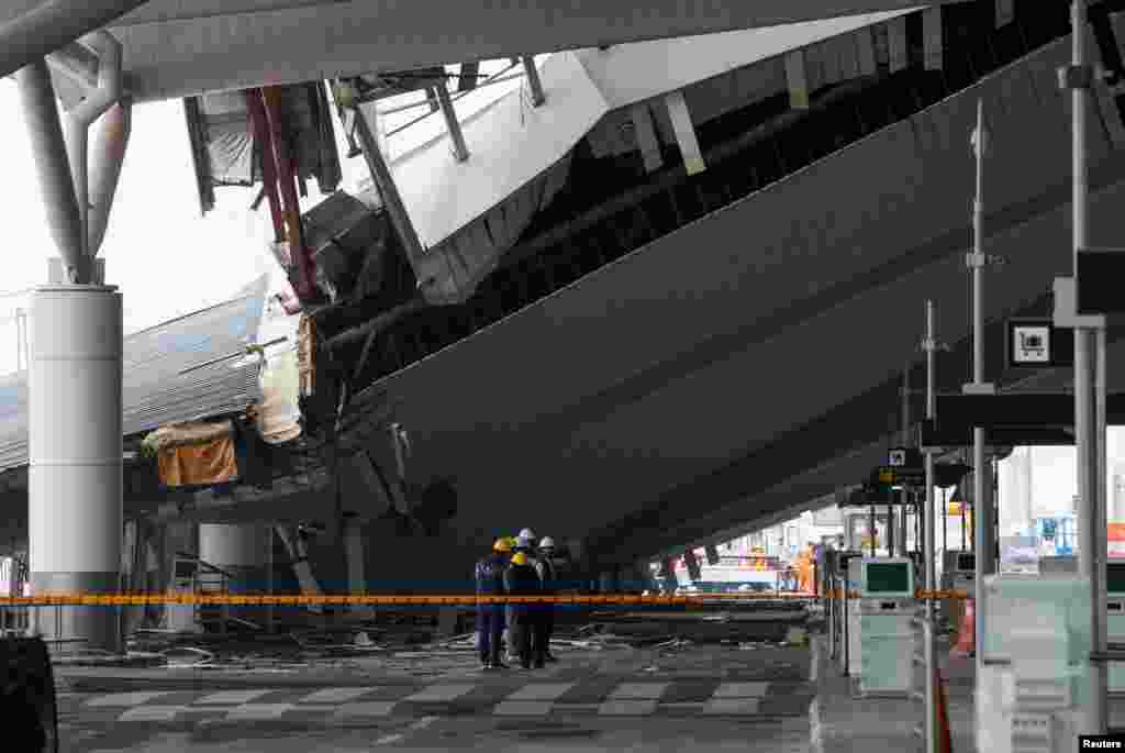Officials from the Forensic Science Laboratory Delhi stand near the portion of a canopy which collapsed following heavy rainfall, at the Indira Gandhi International Airport in New Delhi, India.