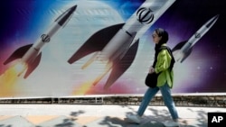 FILE - A woman walks past a banner showing missiles being launched, in northern Tehran, Iran, April 19, 2024.