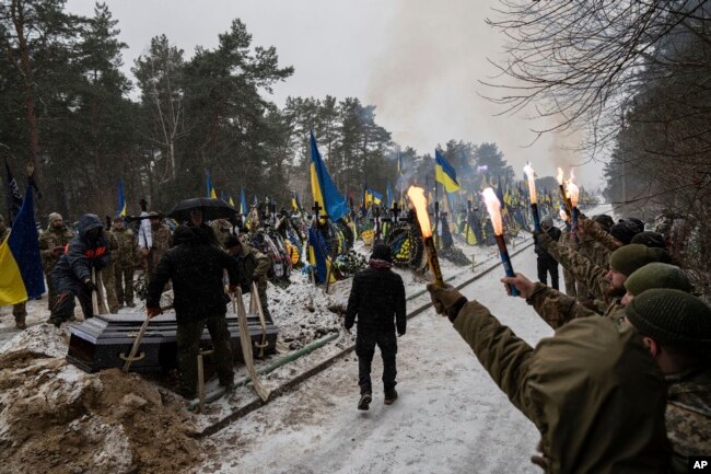 FILE - Funeral workers down a coffin into a grave during a funeral ceremony of Sviatoslav Romanchuk, Ukrainian serviceman, at the cemetery in Kyiv, Jan. 3, 2024.