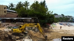 A tourist stands next to a tractor clearing an area after thirteen people, including a Russian couple, died in a mudslide on the Thai resort island of Phuket, Thailand, Aug. 25, 2024. 