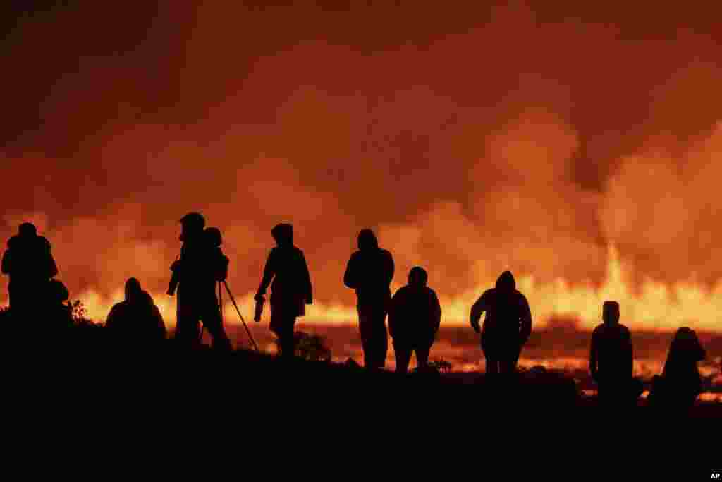 Turis dan pengunjung melihat letusan gunung berapi dari kejauhan di persimpangan antara Reykjanesbraut dan jalan menuju Grindavik di Islandia. (AP)&nbsp;