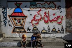Anak-anak Palestina duduk di depan mural bertema Ramadan di Kota Gaza pada 8 Maret 2024. (Foto: AFP)