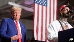 Republican presidential nominee Donald Trump listens as rapper Anuel AA speaks at a campaign event, Aug. 30, 2024, in Johnstown, Pa. Trump is being forced to balance his time on the campaign trail with attention to his multiple criminal trials.