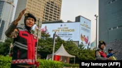 Polisi mengatur arus lalu lintas di dekat baliho bertuliskan selamat datang untuk Paus Fransiskus di Jakarta pada 2 September 2024. (Foto: AFP/Bay Ismoyo)