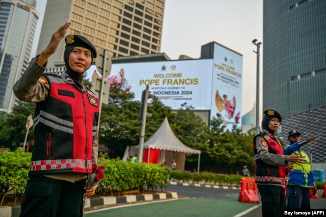 FILE - Polisi mengatur arus lalu lintas di dekat baliho bertuliskan selamat datang untuk Paus Fransiskus di Jakarta pada 2 September 2024. (Bay Ismoyo/AFP)