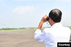 Presiden Jokowi melihat dengan teropong dari jarak jauh simulasi pemberian bantuan lewat udara. (biro setpres)