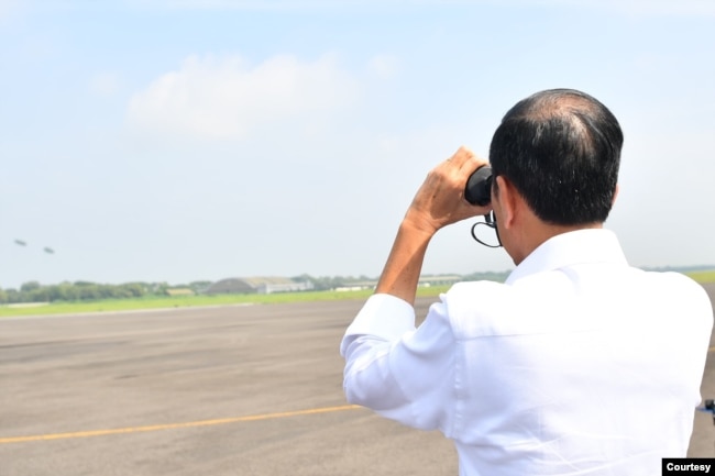 Presiden Jokowi melihat dengan teropong dari jarak jauh simulasi pemberian bantuan lewat udara. (biro setpres)