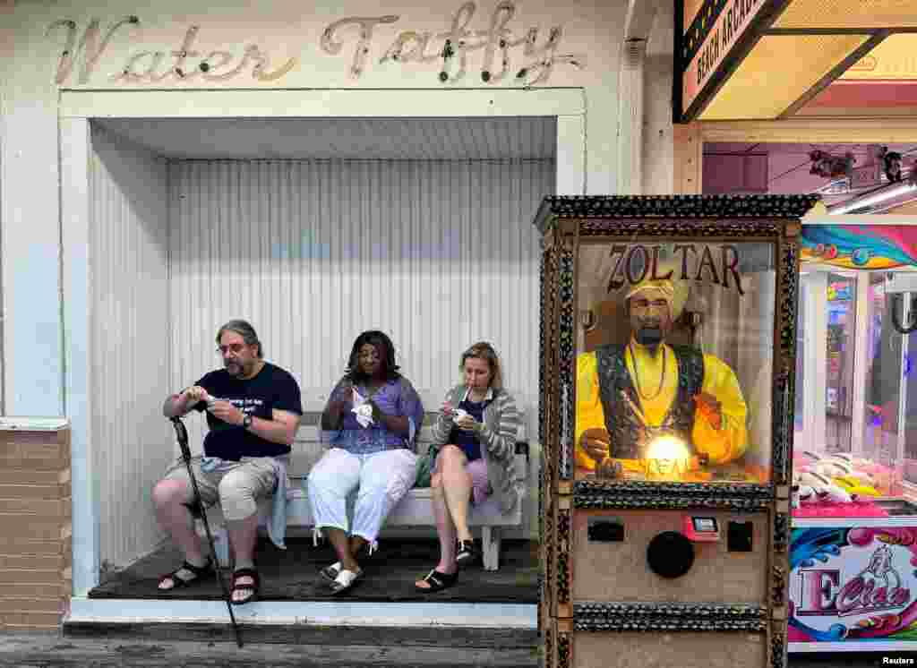 Visitantes del paseo marítimo disfrutan de un helado sentados junto a Zoltar, el adivino, una máquina que funciona con monedas que se hizo famosa en la película &quot;Big&quot;, de Tom Hanks, mientras comienza el fin de semana festivo del Día del Trabajo en Rehoboth Beach, Delaware, EEUU.