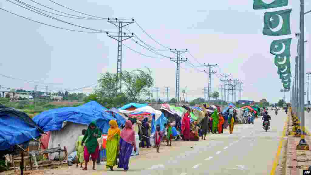 Flood-affected people walk past their makeshift tents along a roadside after heavy monsoon rains in Hyderabad, Sindh province, Pakistan.