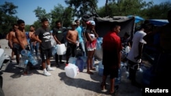 Asylum seekers line up to refill their canisters with drinking water while they wait to attempt to cross into the U.S., at a makeshift camp in Matamoros, Mexico, June 19, 2023.