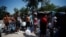 FILE - Asylum-seekers line up to refill their canisters with drinking water while they wait to attempt to cross into the U.S., at a makeshift camp in Matamoros, Mexico, June 19, 2023.
