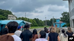 A group of tourists stand near a border station at Panmunjom in the Demilitarized Zone in Paju, South Korea, July 18, 2023. Travis King is fourth from the left, in a dark blue shirt and dark cap.