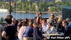 People enjoy drinks and snacks in the evening sun on a terrace overlooking Stockholm, on Tuesday, May 30, 2023. Smoking is prohibited in both indoor and outdoor areas of bars and restaurants in Sweden. (AP Photo/Karl Ritter)
