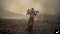 FILE - A man wraps his shirt over his face as he tries to extinguish a fire, near the seaside resort of Lindos, on the Aegean Sea island of Rhodes, southeastern Greece, on July 24, 2023. 