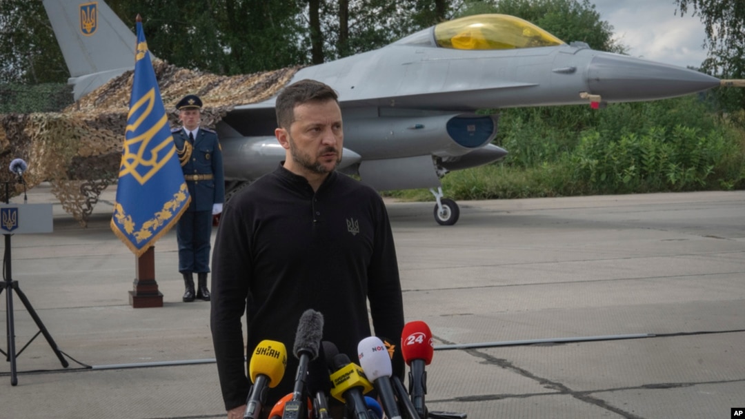 FILE - Ukraine's President Volodymyr Zelenskyy answers reporters' questions with a Ukrainian Air Force F-16 fighter jet in the background, in an undisclosed location in Ukraine, Aug. 4, 2024.