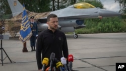 FILE - Ukraine's President Volodymyr Zelenskyy answers reporters' questions with a Ukrainian Air Force F-16 fighter jet in the background, in an undisclosed location in Ukraine, Aug. 4, 2024.