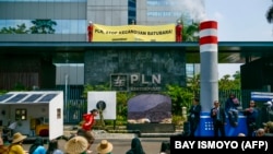 Aktivis lingkungan menggelar aksi teatrikal dan membentangkan spanduk bertuliskan 'PLN, berhenti kecanduan batu bara' sebagai protes terhadap kebijakan PLN terhadap batu bara di Jakarta pada 26 Oktober 2023. (Foto: BAY ISMOYO/AFP)