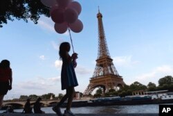 Jenna Baltes, 8, of St. Paul, Minn., holds balloons while walking along the Seine river in front of the Eiffel Tower with her family during the 2024 Summer Olympics, July 29, 2024, in Paris.