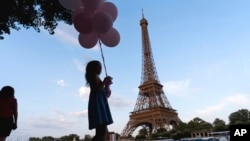 ILUSTRASI - Seorang turis memegang seikat balon, saat berjalan bersama keluarganya di tepian sungai Seine depan menara Eiffel Tower, Paris, 29 Juli 2024.