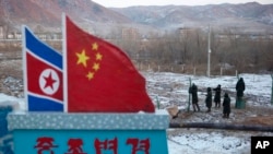 FILE - Chinese paramilitary police build a fence near a concrete marker depicting the North Korean and Chinese national flags with the words "China North Korea Border," at a crossing in Tumen, China, Dec. 8, 2012.