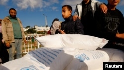 FILE - Palestinians receive sacks of flour distributed by the U.N.’s Palestinian relief agency UNRWA, in Rafah, in the southern Gaza Strip, Nov. 21, 2023.