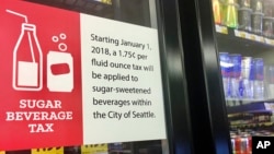 FILE - A sign posted on a drink cooler in a store gives information about a soda tax, in Seattle, Washington, Sept. 24, 2018. The WHO said hiking taxes on sugary drinks could result in healthier populations. 