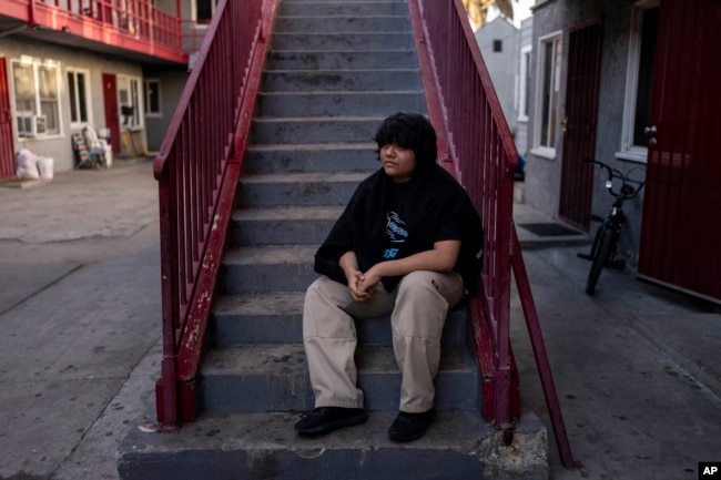 Deneffy Sánchez, 15, sits for a photo in front of a studio apartment his family shares with a retiree originally from El Salvador in Los Angeles, Tuesday, Aug. 29, 2023. (AP Photo/Jae C. Hong)