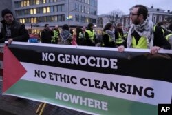 Orang-orang berdiri di depan spanduk di luar Mahkamah Internasional sebelum sidang di Den Haag, Belanda, Jumat, 12 Januari 2024. (AP/Patrick Post)