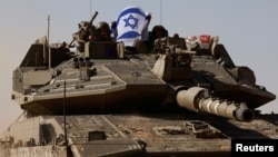 Tentara Israel memegang bendera Israel, saat mereka mengendarai tank Merkava, dekat perbatasan Israel setelah meninggalkan Gaza, selama gencatan senjata sementara antara Hamas dan Israel, di Israel, 24 November 2023. (Foto: REUTERS/Amir Cohen)