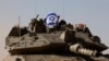 Tentara Israel memegang bendera Israel, saat mereka mengendarai tank Merkava, dekat perbatasan Israel setelah meninggalkan Gaza, selama gencatan senjata sementara di Israel, 24 November 2023. (Foto: REUTERS/Amir Cohen )