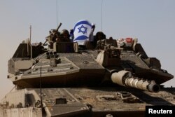 Tentara Israel memegang bendera Israel, saat mereka mengendarai tank Merkava, dekat perbatasan Israel setelah meninggalkan Gaza, selama gencatan senjata sementara antara Hamas dan Israel, di Israel, 24 November 2023. (Foto: REUTERS/Amir Cohen )