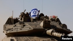 Tentara Israel mengibarkan bendera Israel saat mengendarai tank Merkava di dekat perbatasan antara Israel dan Gaza pada 24 November 2023. (Foto: Reuters/Amir Cohen)