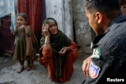 Edema Bibi, 66, sits at the entrance of her house as she speaks with a police officer, during a door to door search and verification drive for undocumented Afghan nationals, in an Afghan Camp on the outskirts of Karachi, Pakistan, Nov. 21, 2023.