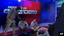 This screen grab of live video from the TC Television network shows a masked, armed person standing over journalists during a live broadcast, in Guayaquil, Ecuador, Tuesday, Jan. 9, 2024. (TC Television network via AP)