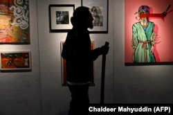 Seorang pengunjung memperhatikan lukisan dalam pameran yang digelar untuk memperingati Hari Internasional Penghapusan Kekerasan Terhadap Perempuan di Banda Aceh, 30 November 2021. (Foto: Chaideer Mahyuddin/AFP)