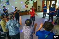 Di bawah kelap-kelip lampu disko, para penderita demensia di rumah lansia Apex Harmony Lodge, Singapura, bergandengan tangan dan menari diiringi lagu-lagu disko tenar jaman dahulu, 12 Mei 2023. (Roslan RAHMAN/AFP)