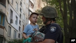 A police officer holds a boy who lost his home after Russia's guided air bomb hit an apartment building in Kharkiv, Ukraine, Aug. 30, 2024.