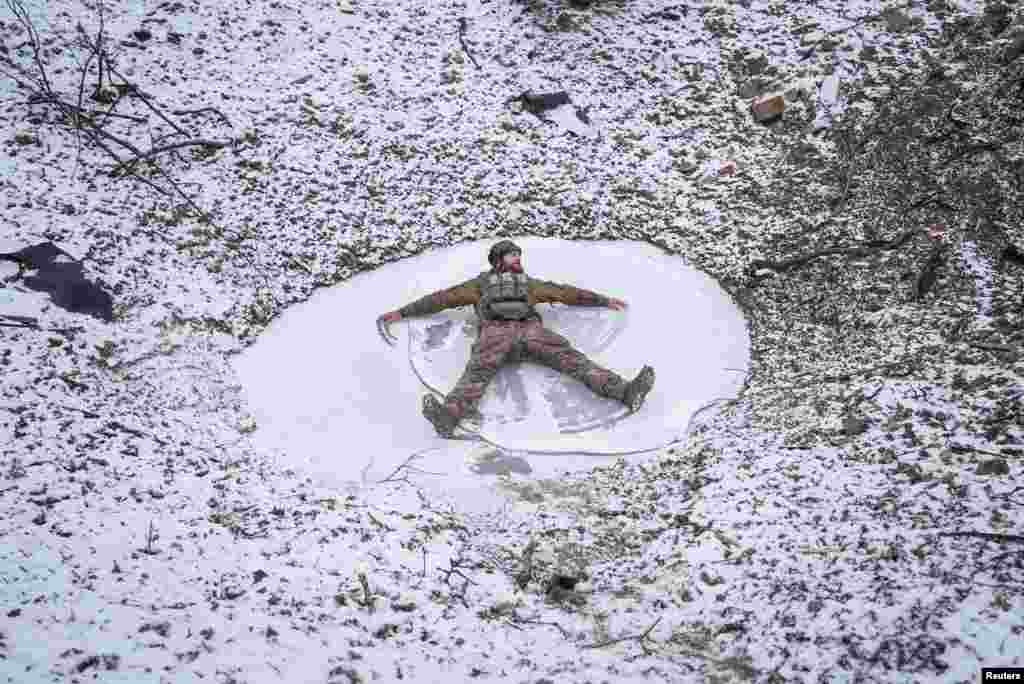 A Ukrainian serviceman of 80th Separate Galician Air Assault Brigade makes a snow angel in a bomb crater, amid Russia's attack on Ukraine, at a position near Bakhmut in Donetsk region, Ukraine, Jan. 25, 2024. 