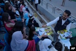 Seorang pria membagikan poster Putra Mahkota Yordania Hussein dan tunangannya, arsitek Saudi Rajwa Alseif, saat konser di stadion olahraga di Amman, Yordania, Senin, 29 Mei 2023. (AP/Nasser Nasser)