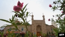 This picture taken on July 19, 2023 shows people passing an old disused mosque in Artux, northwestern China's Xinjiang region. 