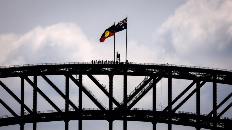 (FILES) Wisatawan berdiri di bawah bendera nasional Aborigin dan Australia yang terletak di atas Jembatan Pelabuhan Sydney pada 27 September 2023, menjelang referendum 